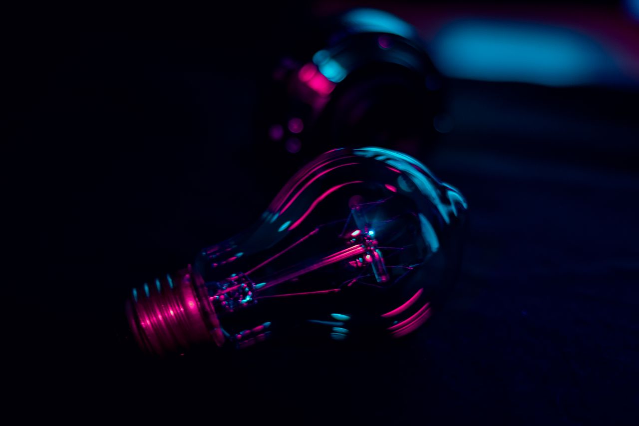 Dramatic close-up of a light bulb illuminated by vibrant neon lighting, evoking a creative and technological ambiance.